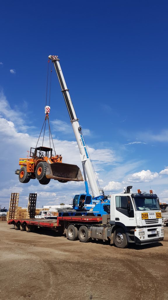 55T Lifting Loader: Crane lifting heavy construction loader onto flatbed truck for transport. Heavy machinery transport.