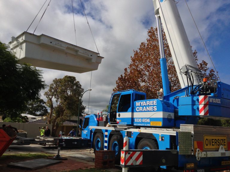 Pool installation with a blue Myaree crane lifting a fiberglass pool shell into place. Professional pool construction.